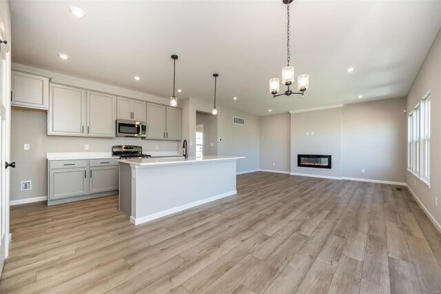 kitchen featuring gray cabinets, light countertops, hanging light fixtures, appliances with stainless steel finishes, and an island with sink