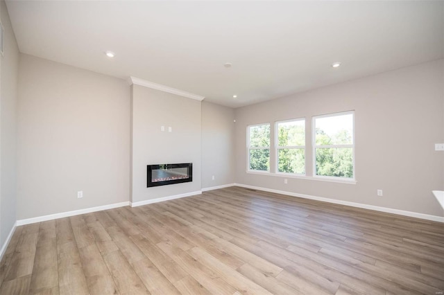 unfurnished living room with light wood-type flooring, recessed lighting, baseboards, and a glass covered fireplace