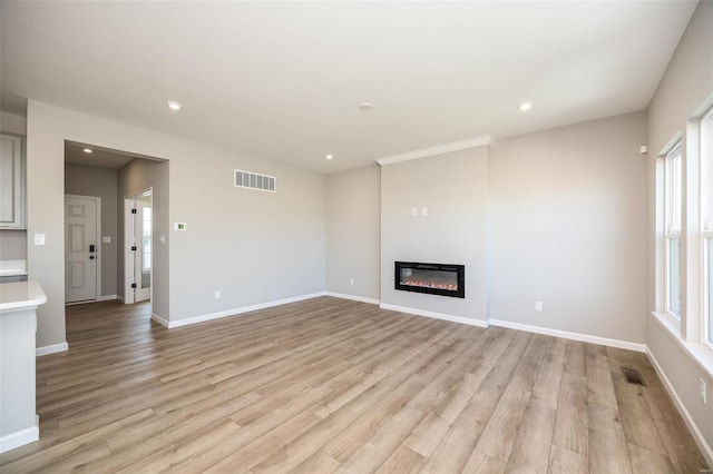 unfurnished living room featuring baseboards, a glass covered fireplace, visible vents, and light wood-style floors