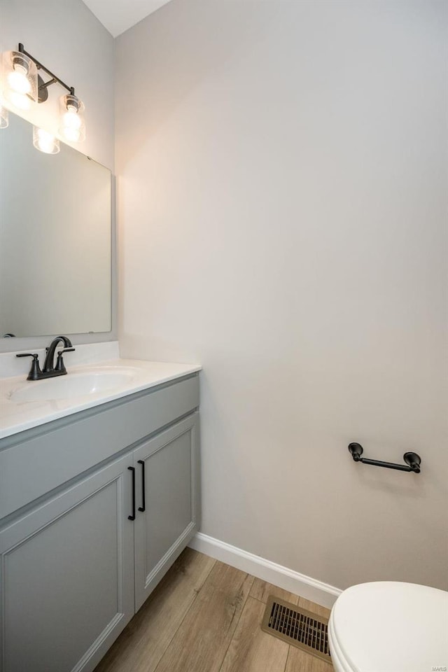 bathroom with visible vents, toilet, vanity, wood finished floors, and baseboards