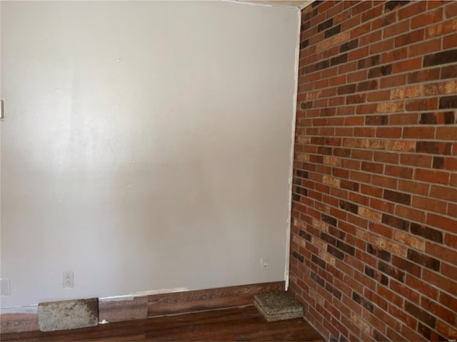 spare room with brick wall and dark hardwood / wood-style flooring