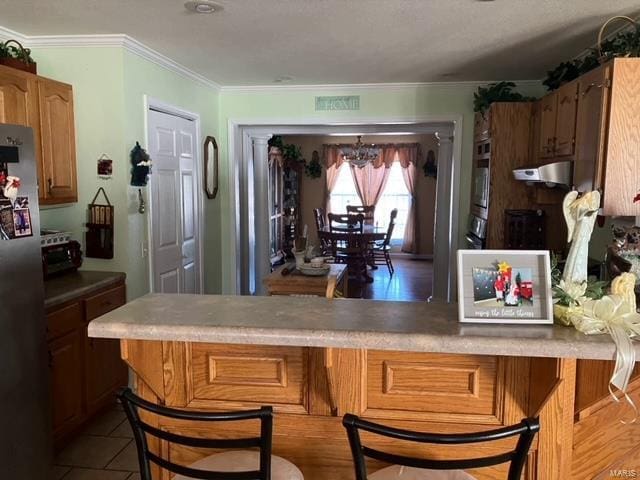 kitchen featuring stainless steel appliances, a kitchen bar, ventilation hood, ornamental molding, and an inviting chandelier