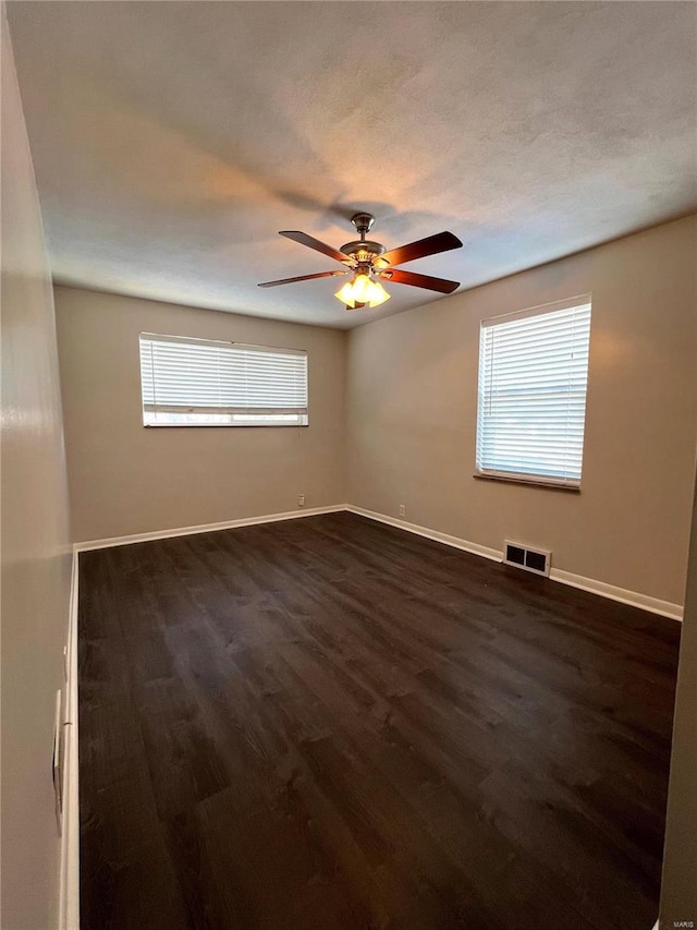 spare room featuring a healthy amount of sunlight, ceiling fan, and dark hardwood / wood-style flooring