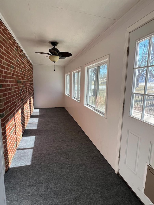 hall featuring brick wall, ornamental molding, and dark colored carpet