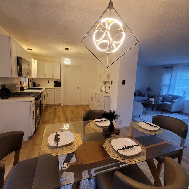 dining room featuring sink, light hardwood / wood-style floors, a textured ceiling, and an inviting chandelier