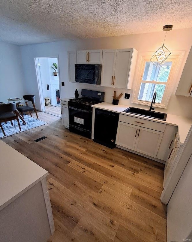 kitchen with light wood-type flooring, sink, black appliances, decorative light fixtures, and white cabinetry