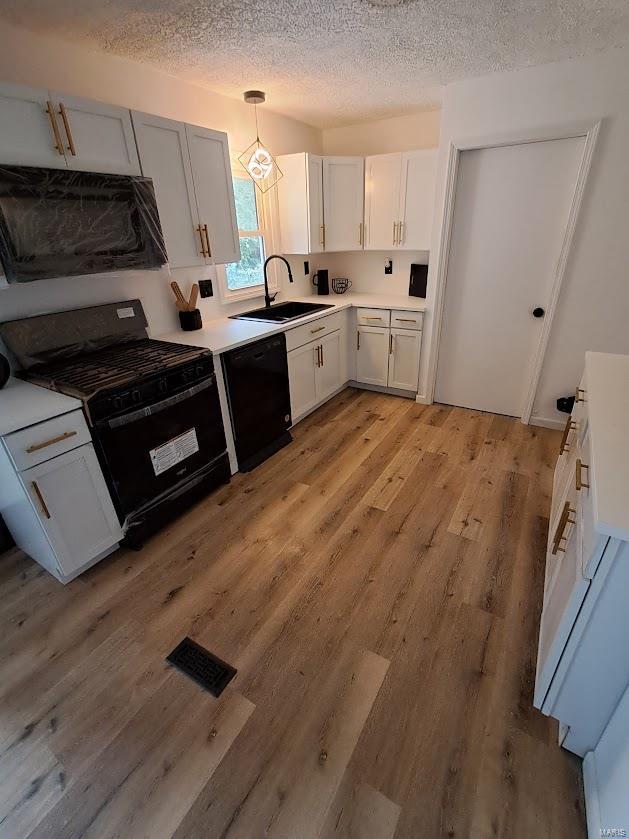 kitchen with light wood-type flooring, sink, black appliances, decorative light fixtures, and white cabinetry