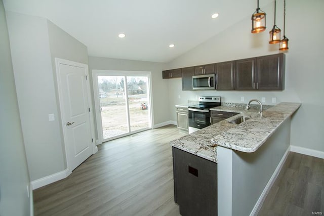 kitchen with appliances with stainless steel finishes, sink, kitchen peninsula, vaulted ceiling, and pendant lighting