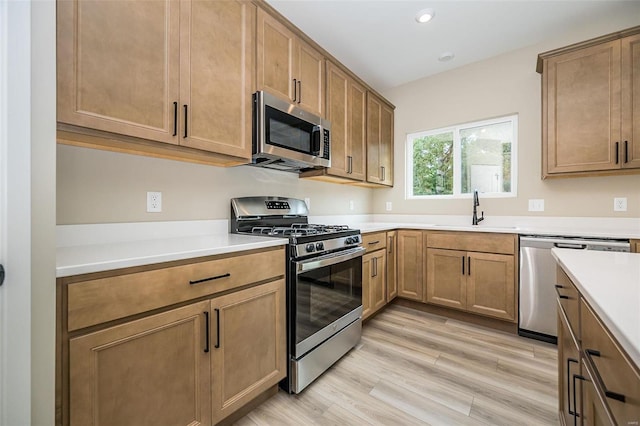 kitchen featuring brown cabinets, light countertops, appliances with stainless steel finishes, a sink, and light wood-type flooring