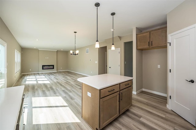 kitchen with brown cabinets, decorative light fixtures, light countertops, a glass covered fireplace, and open floor plan