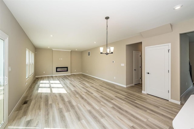 unfurnished living room with a glass covered fireplace, baseboards, light wood finished floors, and an inviting chandelier