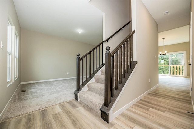 stairway with baseboards, wood finished floors, visible vents, and an inviting chandelier