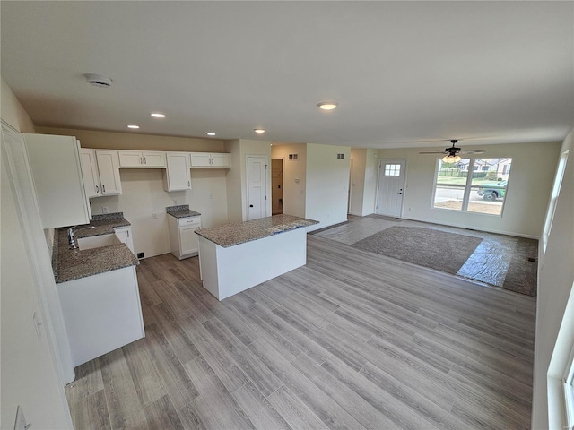 kitchen with light hardwood / wood-style floors, a kitchen island, white cabinets, ceiling fan, and sink