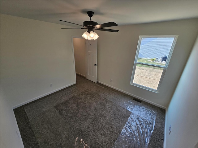 unfurnished room with ceiling fan and dark carpet