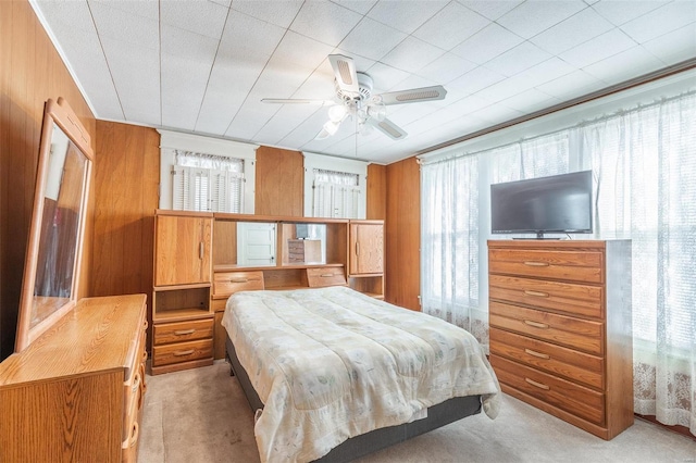 bedroom featuring ceiling fan, wooden walls, and light carpet