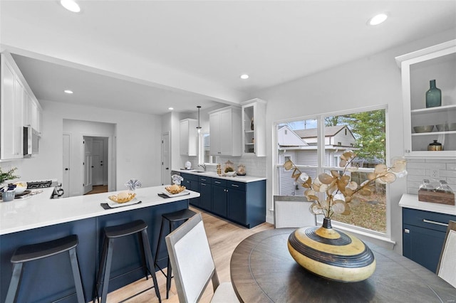 kitchen featuring white cabinetry, a breakfast bar, light hardwood / wood-style flooring, tasteful backsplash, and pendant lighting