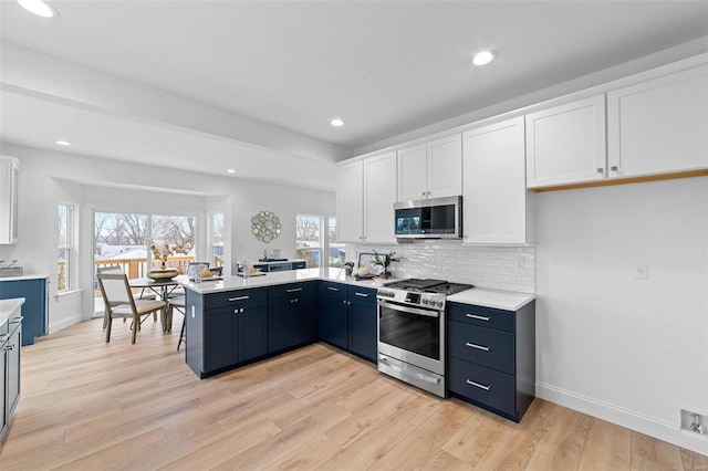 kitchen with tasteful backsplash, stainless steel appliances, white cabinetry, and light hardwood / wood-style flooring