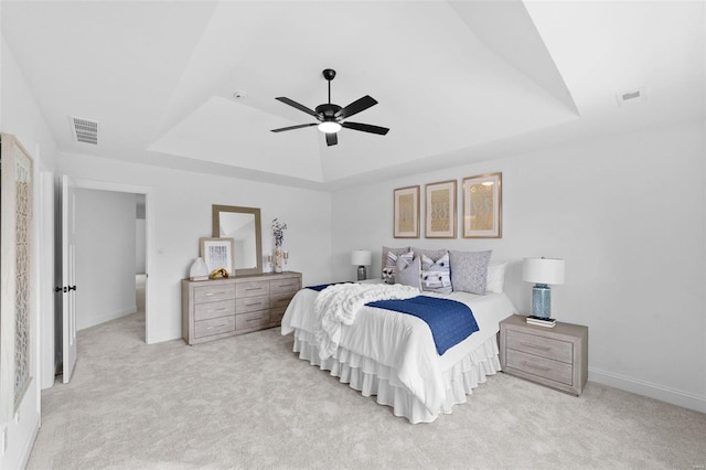 bedroom with light colored carpet, a tray ceiling, and ceiling fan