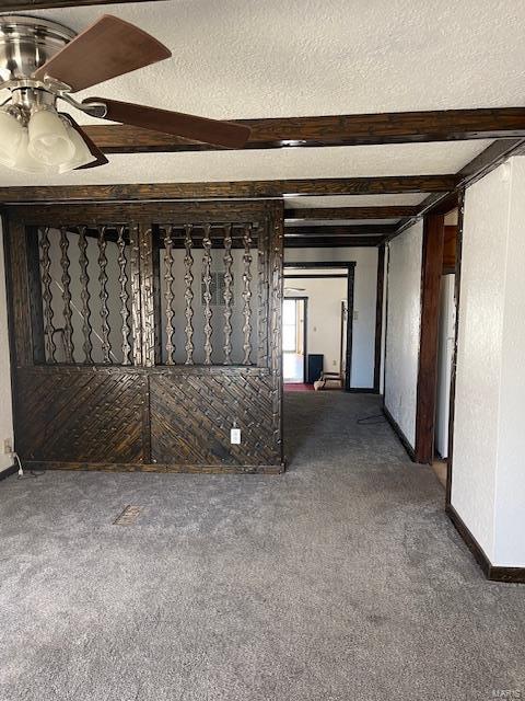 carpeted empty room featuring a textured ceiling, ceiling fan, and beamed ceiling