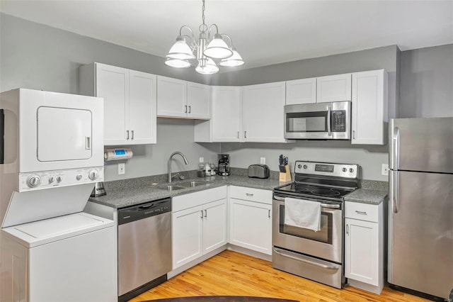 kitchen with stacked washer / dryer, sink, appliances with stainless steel finishes, a chandelier, and light hardwood / wood-style flooring