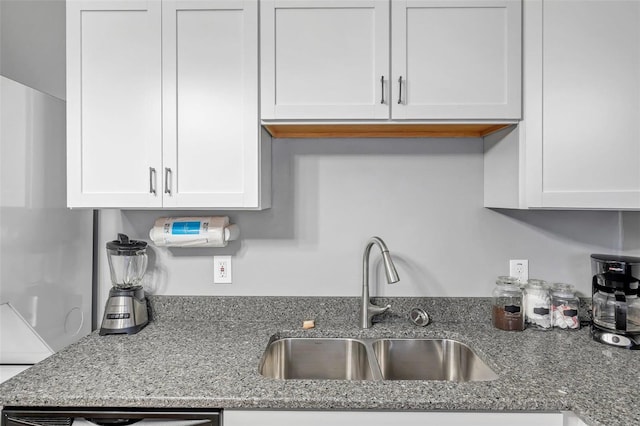 kitchen featuring light stone counters, white cabinetry, and sink