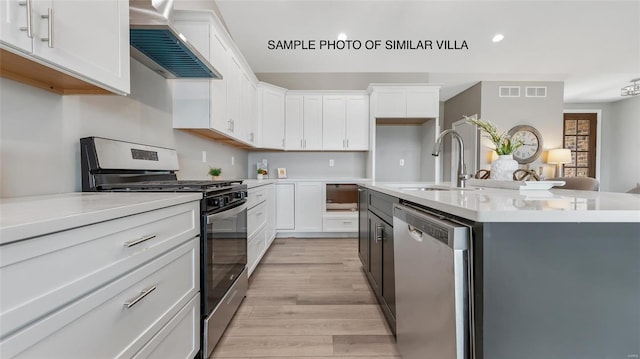 kitchen featuring wall chimney range hood, stainless steel appliances, white cabinetry, and light hardwood / wood-style flooring