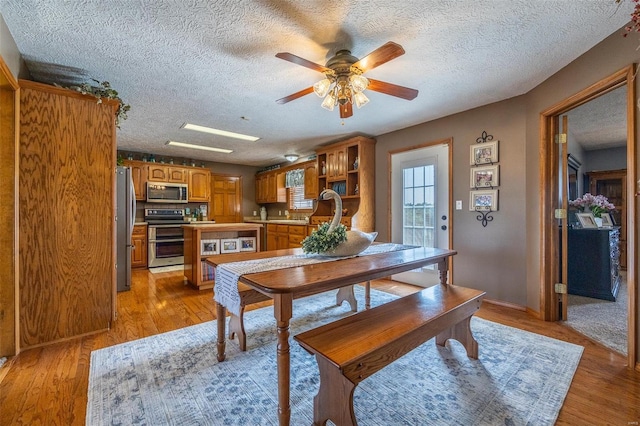 dining area with a textured ceiling, ceiling fan, sink, and light wood-type flooring