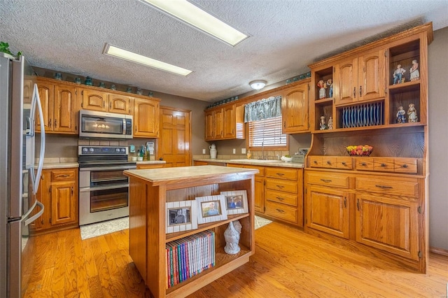 kitchen featuring appliances with stainless steel finishes, sink, light wood-type flooring, a center island, and a textured ceiling