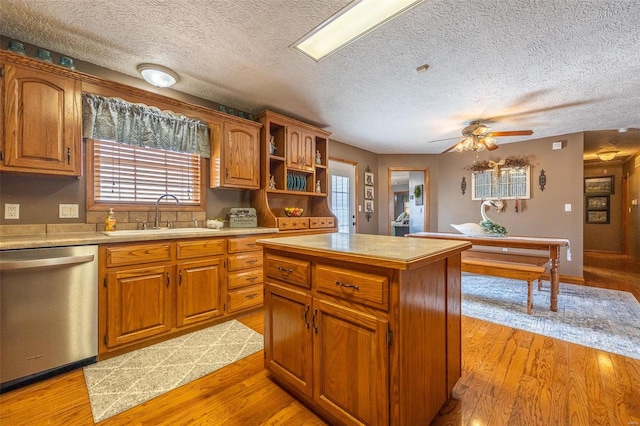 kitchen featuring stainless steel dishwasher, light hardwood / wood-style flooring, a center island, ceiling fan, and sink