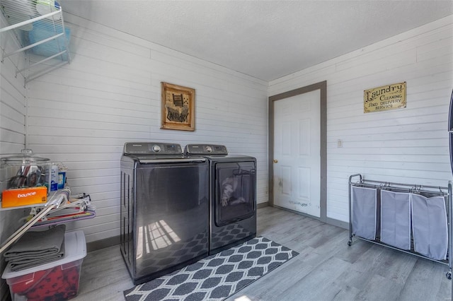 interior space with wood walls, a textured ceiling, washer and dryer, and light wood-type flooring