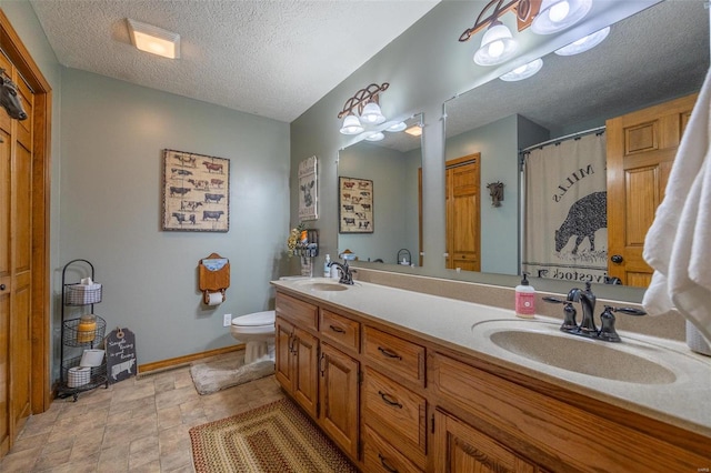 bathroom with dual vanity, tile flooring, toilet, and a textured ceiling