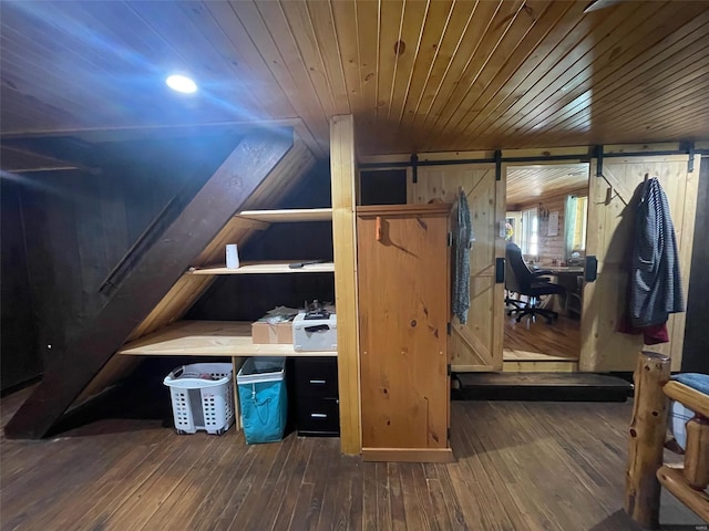 interior space featuring lofted ceiling, wood walls, a barn door, and dark hardwood / wood-style flooring