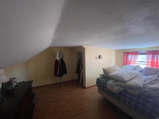 bedroom featuring vaulted ceiling, a textured ceiling, and dark wood-type flooring