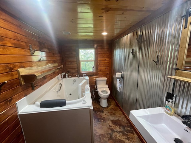 bathroom featuring a bathtub, sink, wood walls, wooden ceiling, and toilet