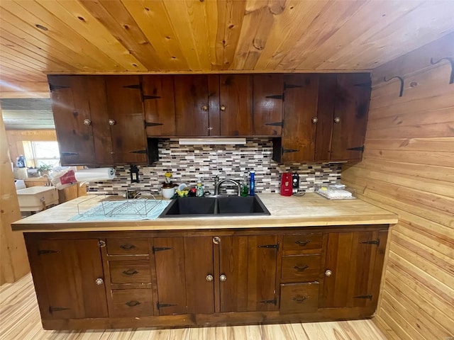 kitchen featuring backsplash, dark brown cabinets, light hardwood / wood-style flooring, wooden walls, and sink