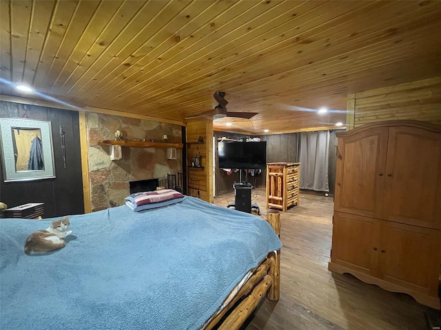 bedroom with wood-type flooring, a fireplace, wooden walls, ceiling fan, and wooden ceiling