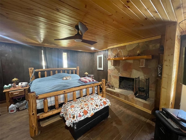 bedroom featuring wood ceiling, dark hardwood / wood-style flooring, wood walls, a stone fireplace, and ceiling fan