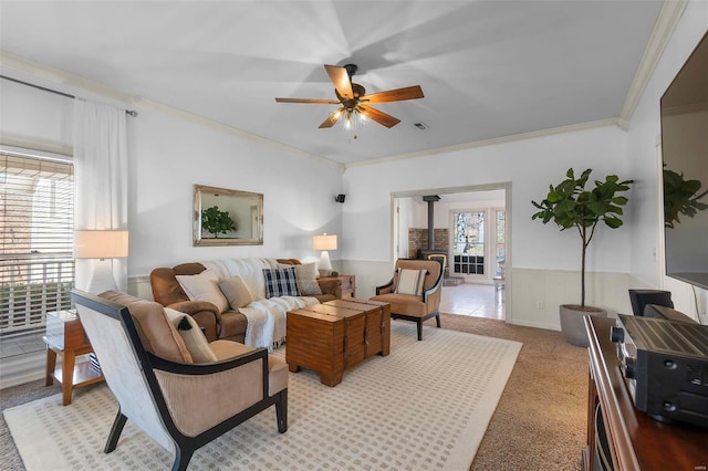 living area featuring visible vents, crown molding, wainscoting, a wood stove, and a ceiling fan