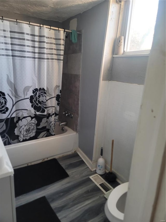 bathroom featuring wood-type flooring, a textured ceiling, toilet, and shower / bath combo with shower curtain