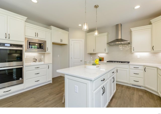 kitchen featuring wall chimney exhaust hood, stainless steel appliances, white cabinets, and light hardwood / wood-style floors