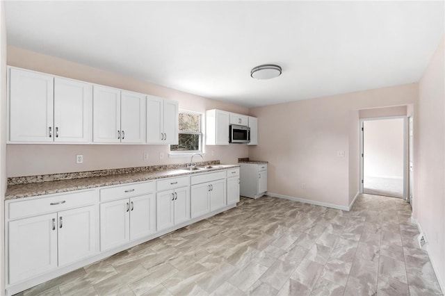 kitchen with light stone countertops, white cabinetry, and sink