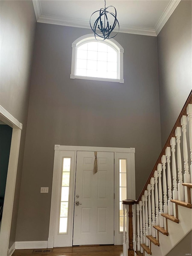 foyer entrance featuring crown molding, a notable chandelier, a towering ceiling, and hardwood / wood-style flooring