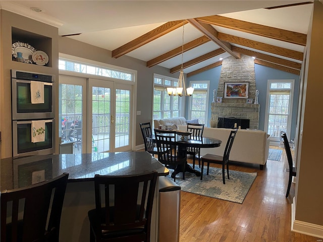 dining space featuring an inviting chandelier, a stone fireplace, beam ceiling, and plenty of natural light