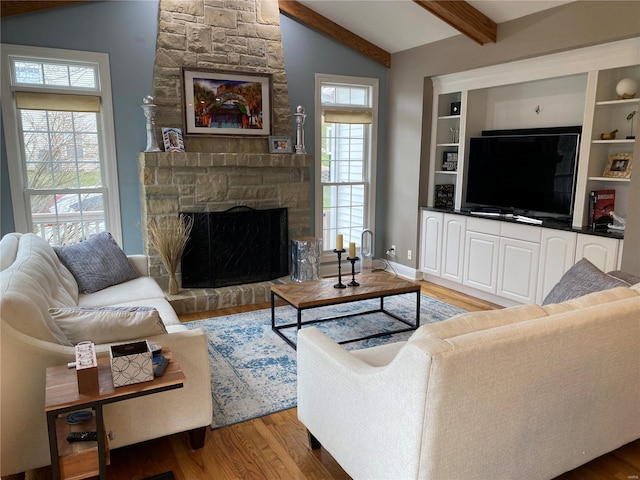 living room with a fireplace, vaulted ceiling with beams, light hardwood / wood-style flooring, and plenty of natural light