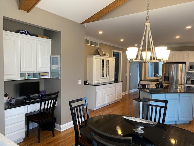 dining space with an inviting chandelier, light hardwood / wood-style floors, built in desk, ornamental molding, and beam ceiling