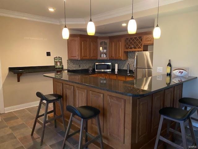 kitchen with a breakfast bar, stainless steel appliances, tasteful backsplash, and dark tile floors