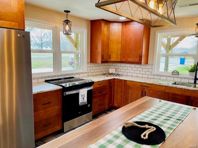 kitchen featuring backsplash, stainless steel appliances, decorative light fixtures, and light stone counters