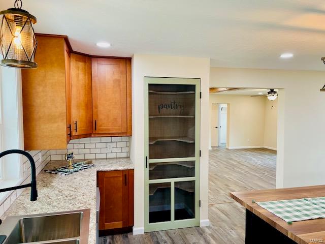 kitchen with decorative light fixtures, tasteful backsplash, light wood-type flooring, light stone countertops, and sink