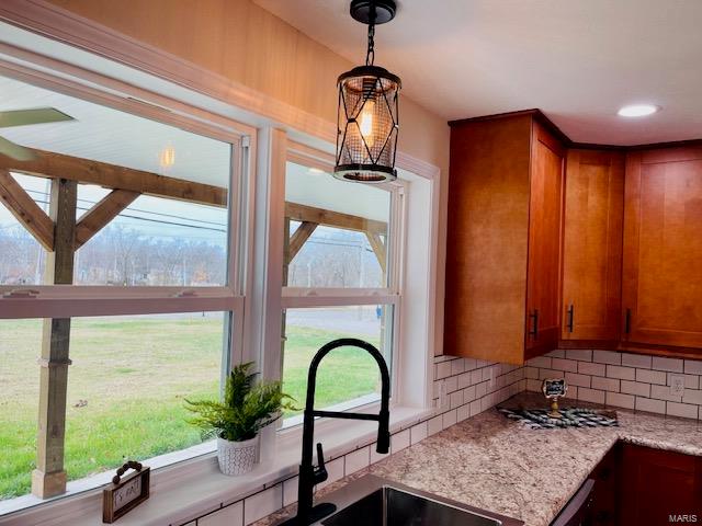 kitchen featuring pendant lighting, an inviting chandelier, light stone countertops, backsplash, and sink