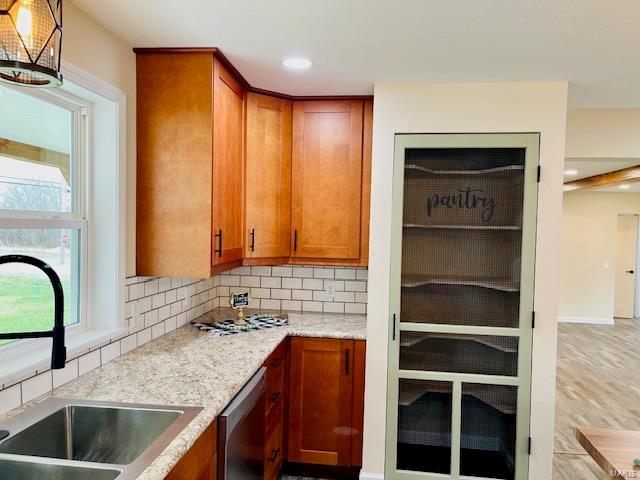 kitchen with sink, light stone counters, dishwasher, backsplash, and light wood-type flooring